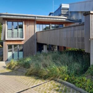 Zeitgemäße Holz-Aluminium-Fenster in einer modernen Gebäudearchitektur mit Holzfassade und verbindendem Steg – großformatige Fensterflächen für hohe Lichtdurchlässigkeit und klare Fassadengestaltung.